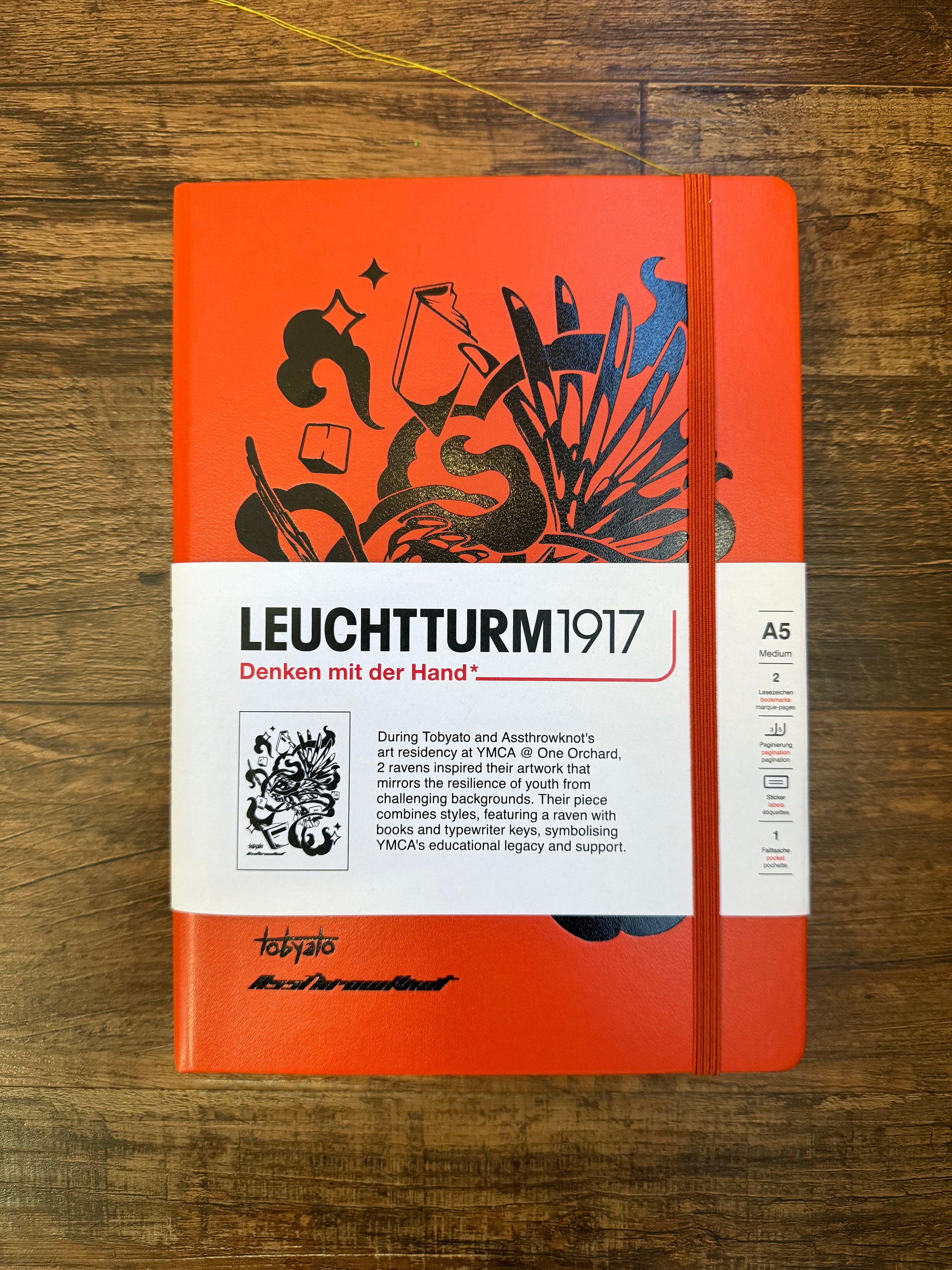 Leuchtturm1917 Tobyato Edition A5 Medium Notebook in fox red with dotted pages, featuring a cover design of a raven with books and typewriter keys, symbolizing knowledge and resilience.